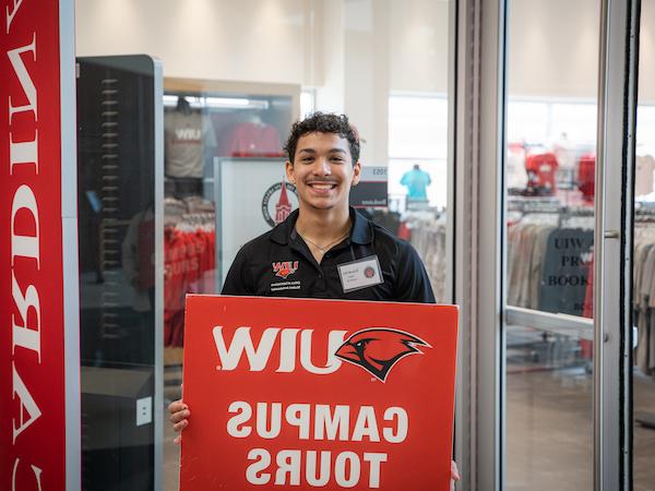 student holding a sign reading UIW campus tours